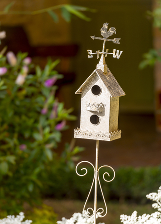 Decorative white birdhouse in a flower garden with classic weather vane on topの写真素材