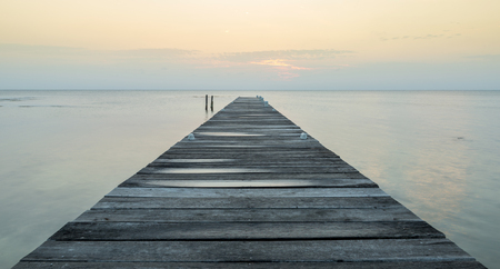 Dawn on a wooden jetty stretching into the silent oceanの写真素材