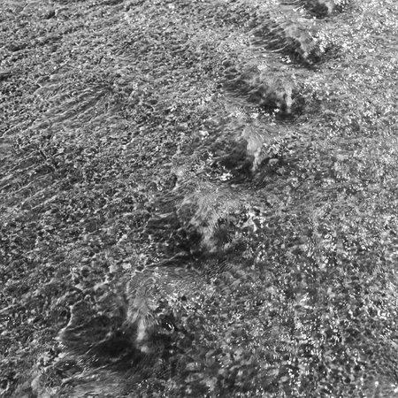 Sunlight on running tannin water ripple background in black and white