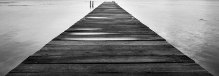 Dawn on a wooden jetty stretching into the silent ocean in stunning black and whiteの写真素材
