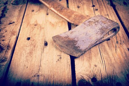 An old hatchet axe with a wooden handle and wear marks sits on a rough timber background with retro style filter effectの写真素材
