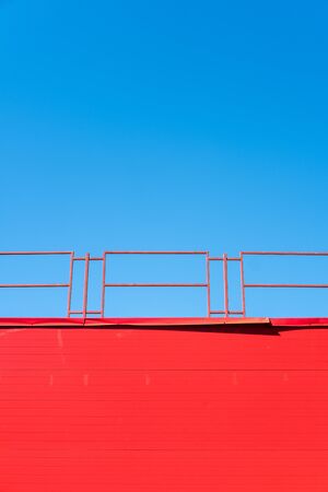 Red wall with a fence on a blue sky backgroundの写真素材