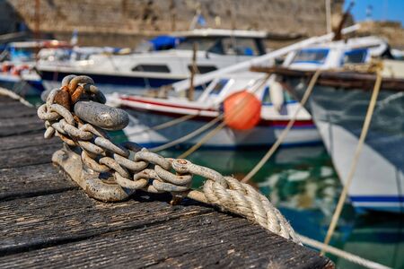 Metal mooring bollard on a wooden pier with moored yachtsの写真素材