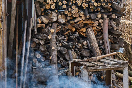 Old ax lying on the background of a stack of firewood next to the smoking barbecue
