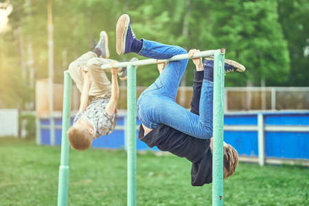 Boys in casual clothes hanging upside down on bars while playing together on summer day in schoolyardの写真素材