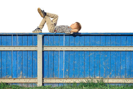 Side view of relaxed boy in casual clothes lying on blue hockey rink fence and dreaming against white backgroundの写真素材