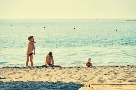 Boys and baby playing with sand on coast near sea in summer morning on resortの写真素材