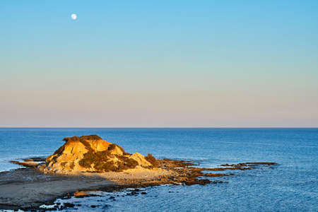 Small island with hill located in rippling sea against cloudless sundown sky in evening in countrysideの写真素材