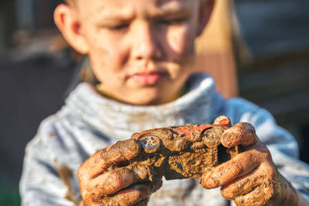 Angry boy looking at a dirty car after playing in the sandbox near wooden rural house in summer day in countrysideの写真素材
