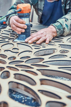 Decorative partition wall manufacturing process. Carpenter milling holes in MDF with a hand electric...