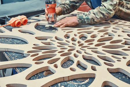 Decorative partition wall manufacturing process. Carpenter milling holes in MDF with a hand electric router machine. Decorative partition wall with floral pattern.の写真素材