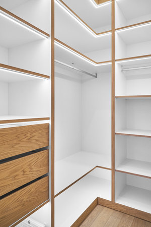 Elegant white shelving with LED lighting. Shelving of laminated boards with edges and faces of drawers made of oak veneer plywood sheets in walk-in closetの写真素材
