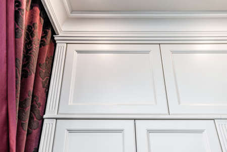 Classical style white wardrobe against the background of burgundy curtains with a floral pattern closeup viewの写真素材