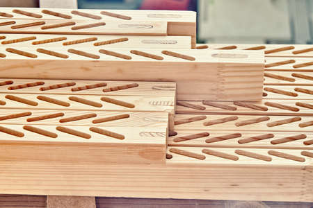 New processed wooden bars with lines of slots to install thin planks lie on workbench in light...