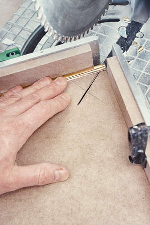 Worker cutting golden molding decorative strip for furniture facade panel on miter saw during...