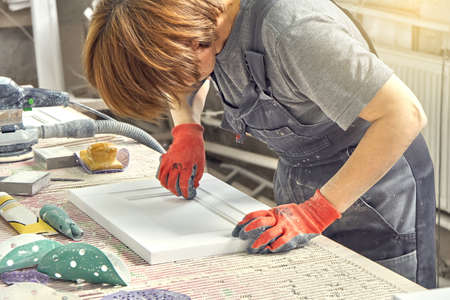 Female employee in dirty uniform and working gloves polishes wooden part of furniture facade at...
