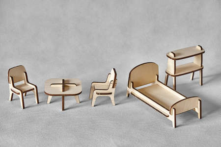 Cute small toy bed, armchairs, table and shelf made of ply wood details cut with laser machine tool stand on light gray backgroundの写真素材