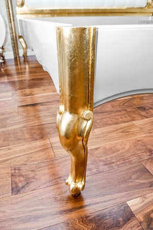 Stylish antique turning leg of bed covered with shiny golden paint on parquet floor in brightly lit room extreme close viewの写真素材