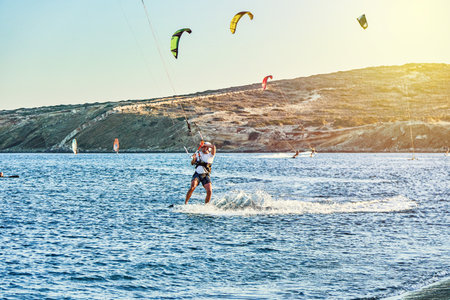 Rhodes, Greece - July 08 2017: Strong sportsmen goes kitesurfing on tranquil azure sea water on Prasonisi beach at sunset on clear horizon in Greece in summer eveningのeditorial素材