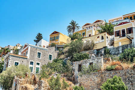 Multicolored historical buildings in old town scattered on hills on Symi island on sunny day in...