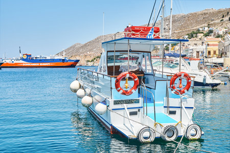 Symi, Greece - July 05 2017: Moored motorboats on azure sea with reflection against historical...