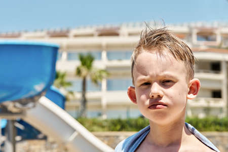 Portrait of funny boy with towel near the water slides at tropical resort on sunny dayの写真素材