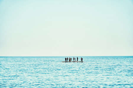 Silhouettes of people tourists waiting for rescue standing on small island in tranquil ocean under...