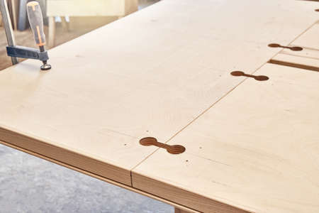 Part of new large wooden dining table with insert holes for worktop connectors in light workshop of...
