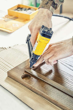 Skilled carpenter assembles wooden door for kitchen cabinet fixing glazing bead with pins from pneumatic stapler closeupの写真素材