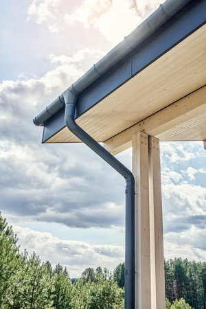 Contemporary gray metal rainwater downpipe installed on roof of new building with wooden terrace on...