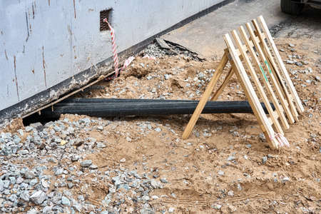 New plastic water pipes digging under old apartment building covered with small wooden fence at repairing works on spring dayの写真素材