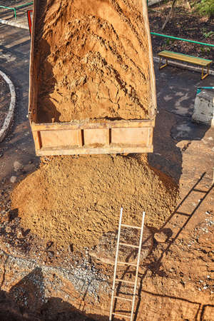 Old tipper truck pours out pile of soil near trench with ladder in dwelling building yard at water...