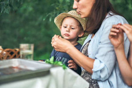 Young mother and little son in straw hat with food sit at table during picnic in green park on nice summer day close viewの写真素材