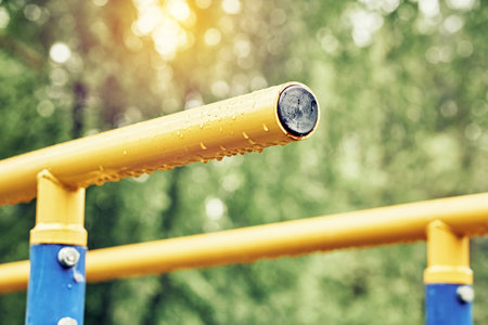 Yellow metal bars for exercises with hanging rain drops at sports ground in spring green park on cloudy day extreme close viewの写真素材