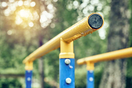 Yellow metal bars for exercises with hanging rain drops at sports ground in spring green park on cloudy day extreme close viewの写真素材