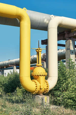 Large water shutoff valve with flanges and lever on pipeline system in green bushes against clear blue sky on sunny spring dayの写真素材