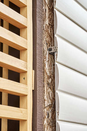 Elegant wooden grid divider near wall of cottage covered with contemporary white plastic siding on...