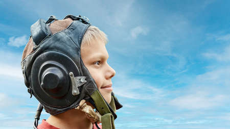 Profile view of positive teenage boy wearing vintage leather pilot helmet against of cloudy sky background close viewの写真素材