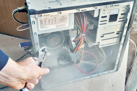 Employee cleans an open old computer with air duster cleaning spray gun in the workshop closeup