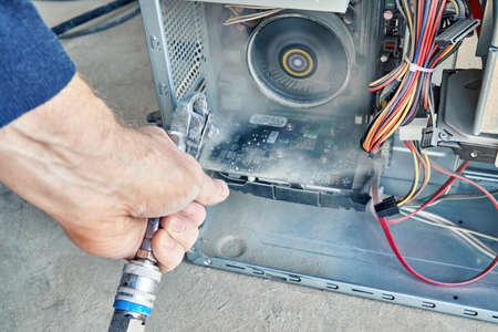 Employee cleans an open old computer with air duster cleaning spray gun in the workshop closeupの写真素材