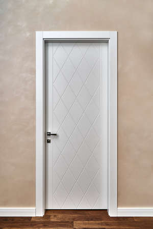 Stylish contemporary white door decorated with rhombus pattern in light room with painted beige wall and wooden parquet floorの写真素材