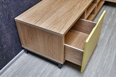 Elegant TV stand made of oak wood veneer with bright yellow facade and open drawers in minimal style near dark cork wall in living roomの写真素材