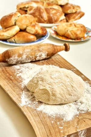Wooden cutting board with raw dough for pies from wheat flour and vintage rolling pin on white table...