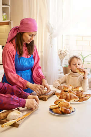 Positive woman in Udmurt national costume kneads dough cooking pies with mature mother while the...