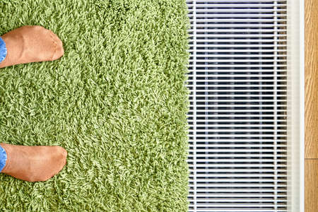 Contemporary water underfloor heat convector installed near panoramic window with green carpet and feet in orange socks upper viewの写真素材