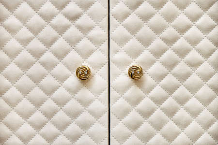 Elegant wardrobe facades covered with light beige alcantara quilted by rhomb pattern and decorative golden knobs close viewの写真素材
