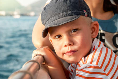 Cute toddler with mother enjoys boat trip sailing in sea past coast of Marmaris. Portrait of boy in sun-protective cap on vacation in Turkey closeupの写真素材