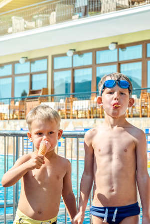 Cute blond boys eat ice cream standing near swimming pool in hotel of Marmaris. Tanned toddler and...