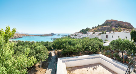 Lindos, Greece - July 08 2017: Ancient Lindos city on Rhodes island with view on Acropolis. White houses with private green gardens scattered on sea bay coast with turquoise waterのeditorial素材