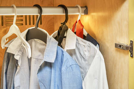 Children wardrobe with LED lighting and clothes on hangers. Yellow plywood cabinet with open door. Modern furniture for room interior closeupの写真素材